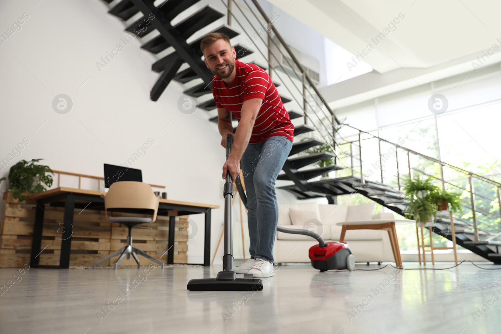 Photo of Young man using vacuum cleaner in living room