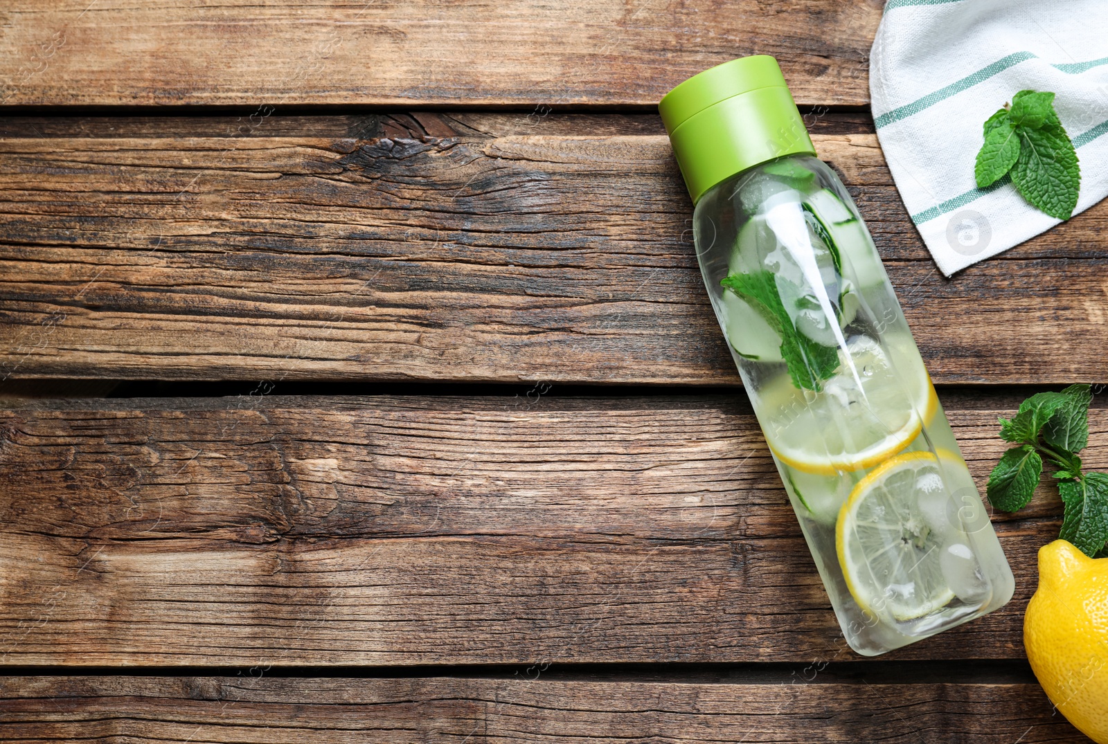 Photo of Bottle of refreshing water with cucumber, lemon and mint on wooden table, flat lay. Space for text