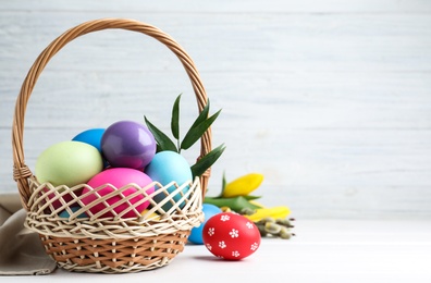 Photo of Colorful Easter eggs in wicker basket and flowers on white background. Space for text