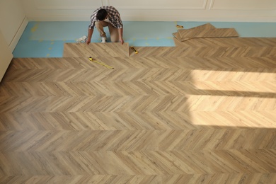 Photo of Professional worker installing new parquet flooring indoors, above view