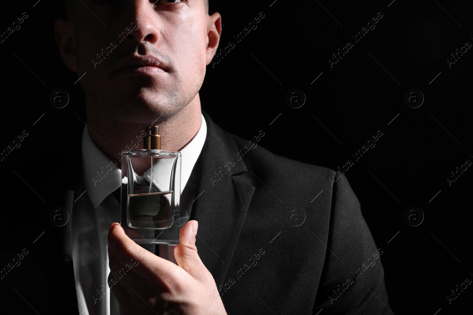 Photo of Man holding bottle of luxury perfume on black background, closeup