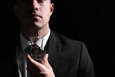 Photo of Man holding bottle of luxury perfume on black background, closeup