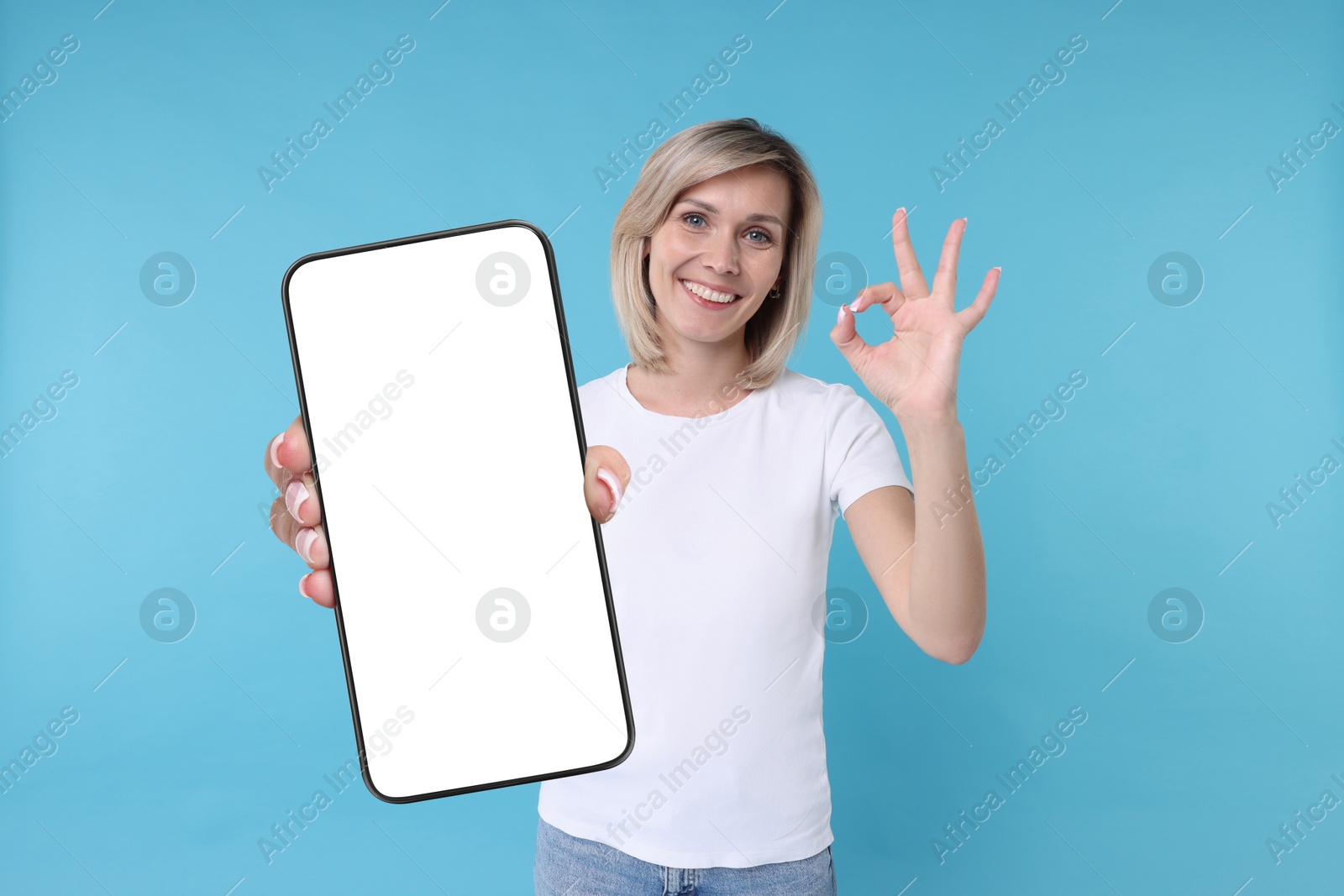 Image of Happy woman showing mobile phone with blank screen on light blue background. Mockup for design