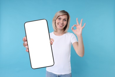 Happy woman showing mobile phone with blank screen on light blue background. Mockup for design