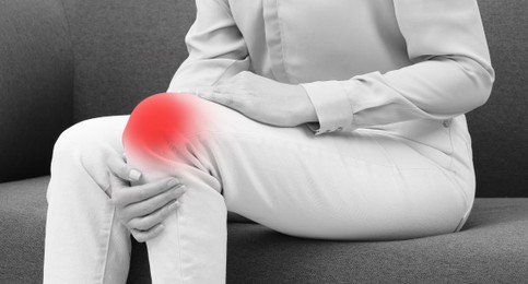 Image of Woman suffering from pain in knee on sofa, closeup. Black and white effect. Banner design