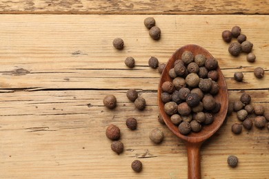 Photo of Aromatic allspice pepper grains in spoon on wooden table, top view. Space for text