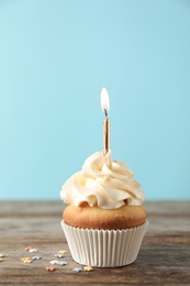 Delicious birthday cupcake with burning candle on color background