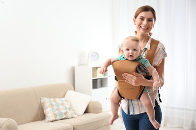 Woman with her son in baby carrier at home. Space for text