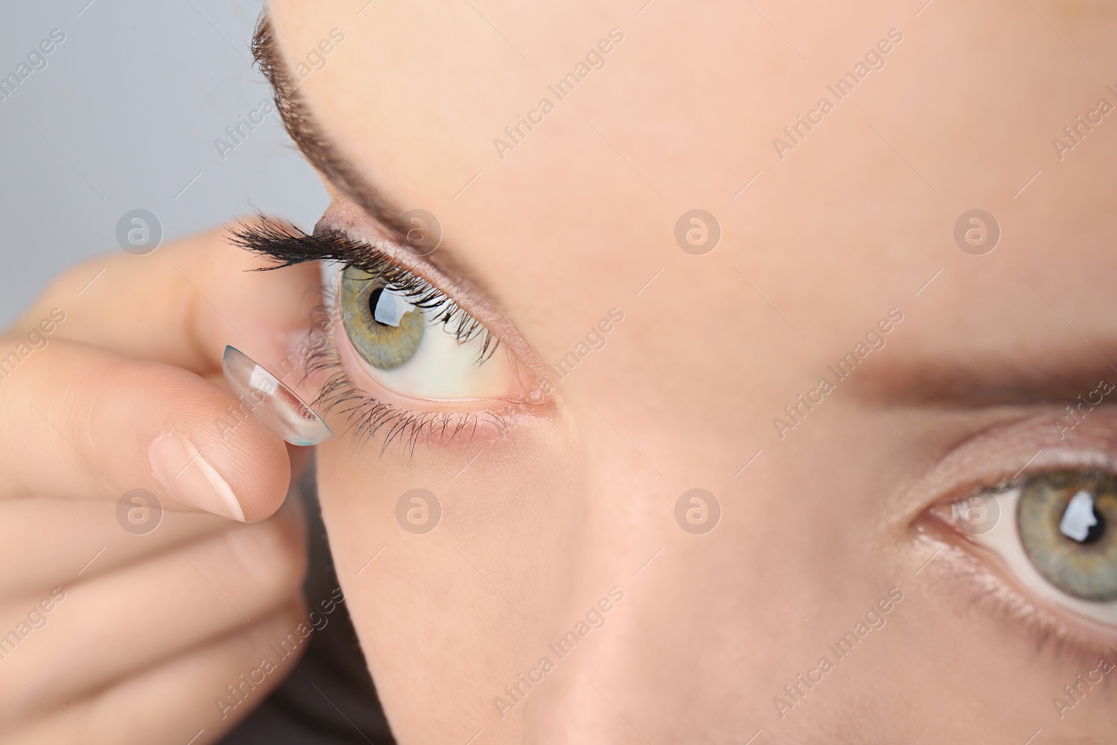 Photo of Young woman putting contact lens in her eye, closeup