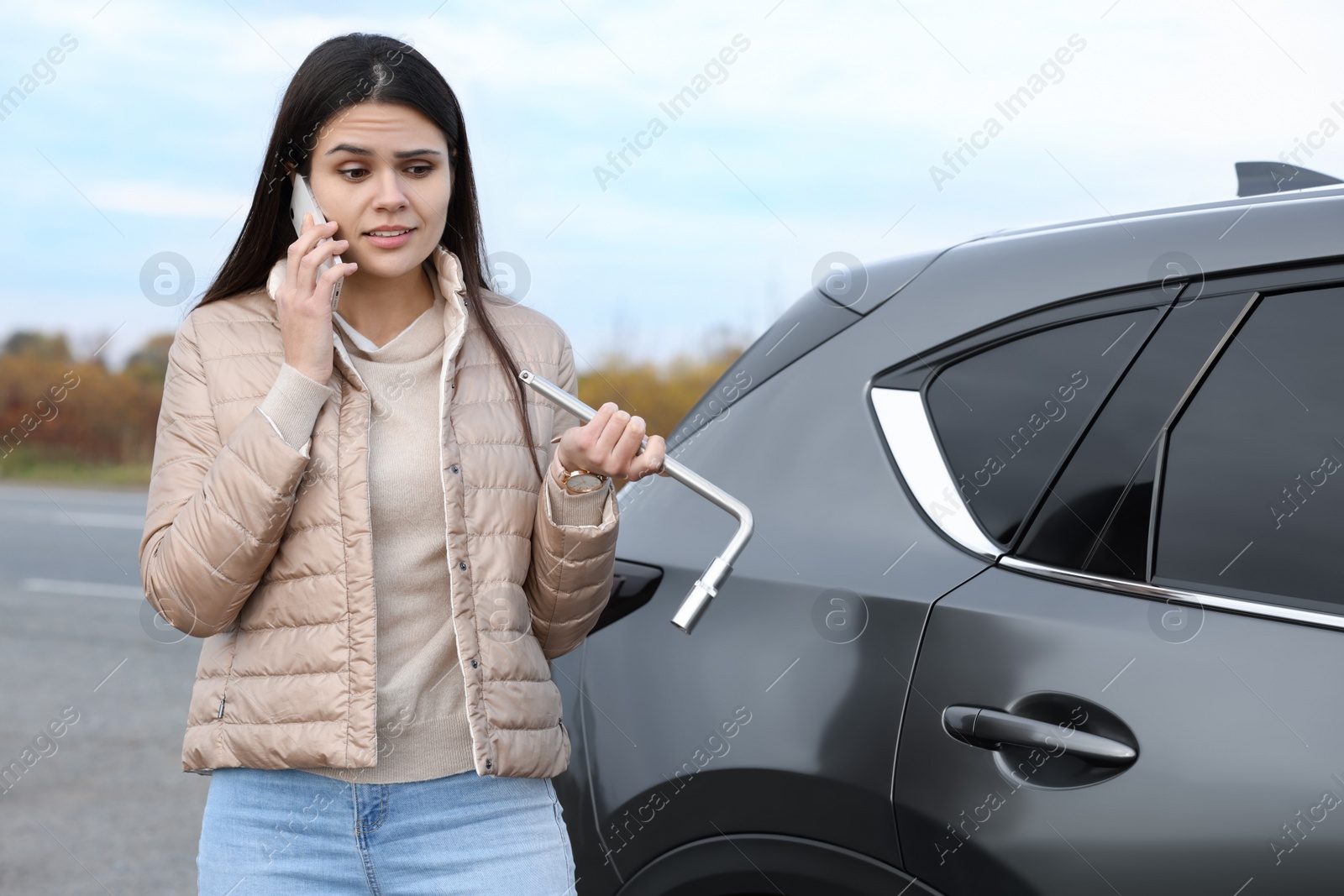 Photo of Worried young woman calling car service. Tire puncture