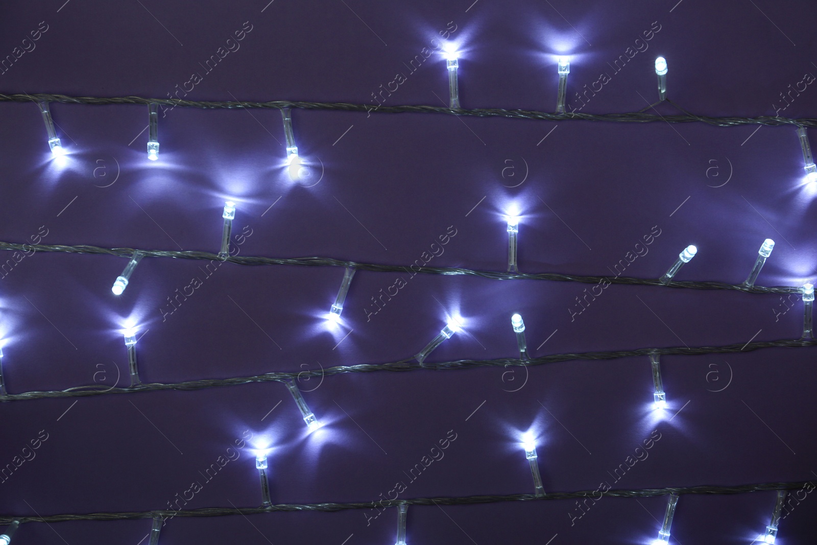 Photo of Glowing Christmas lights on dark violet background, top view