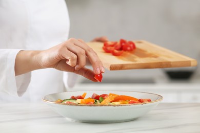 Photo of Professional chef adding cut tomato into delicious salad at white marble table, closeup
