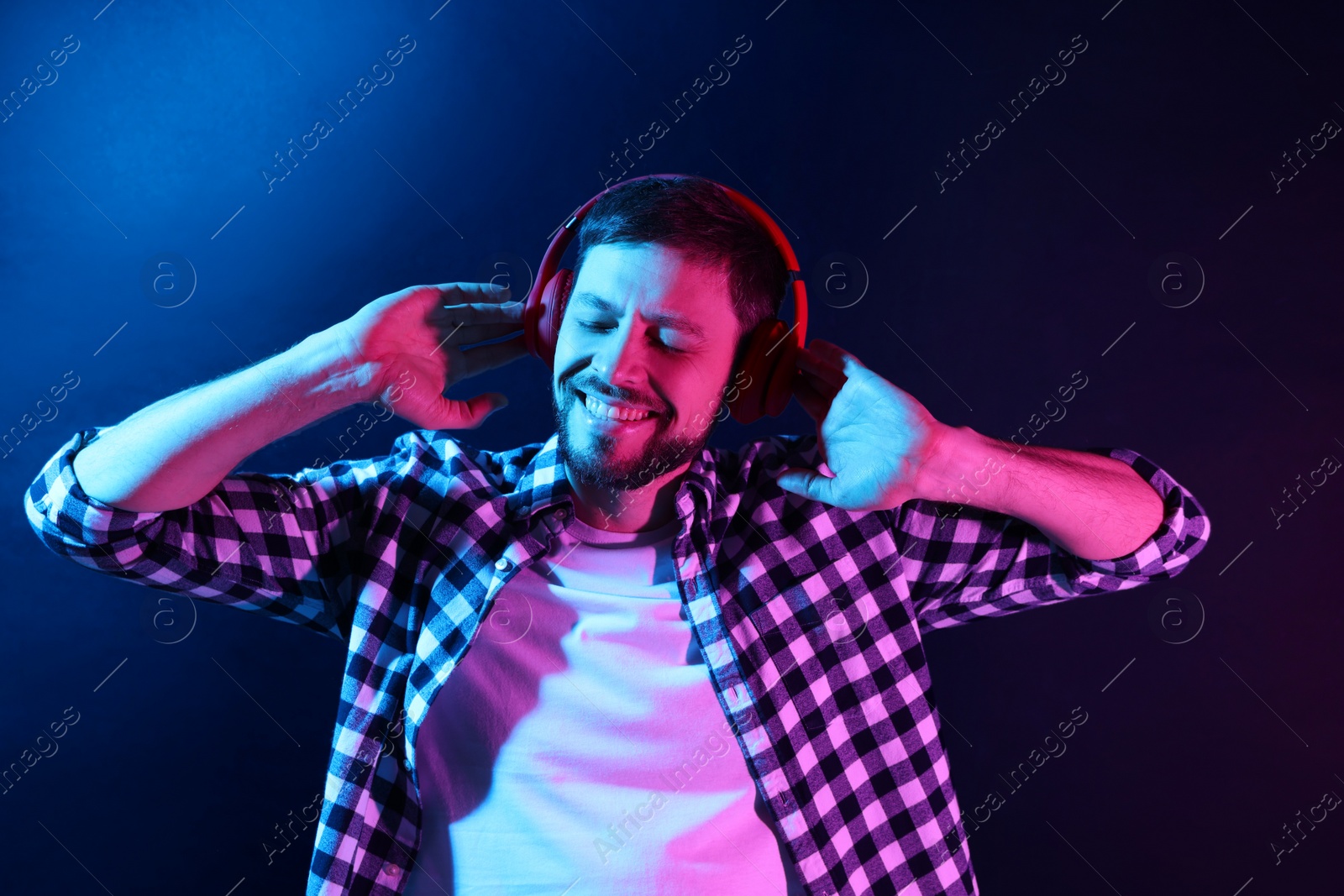 Photo of Happy man in headphones enjoying music in neon lights against dark blue background