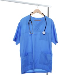 Photo of Light blue medical uniform and stethoscope on rack against white background