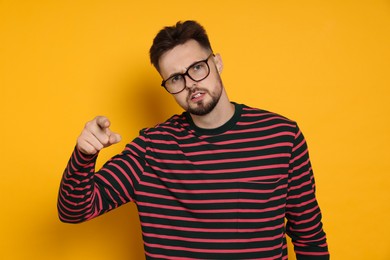 Photo of Aggressive man in striped sweatshirt and eyeglasses pointing at something on yellow background