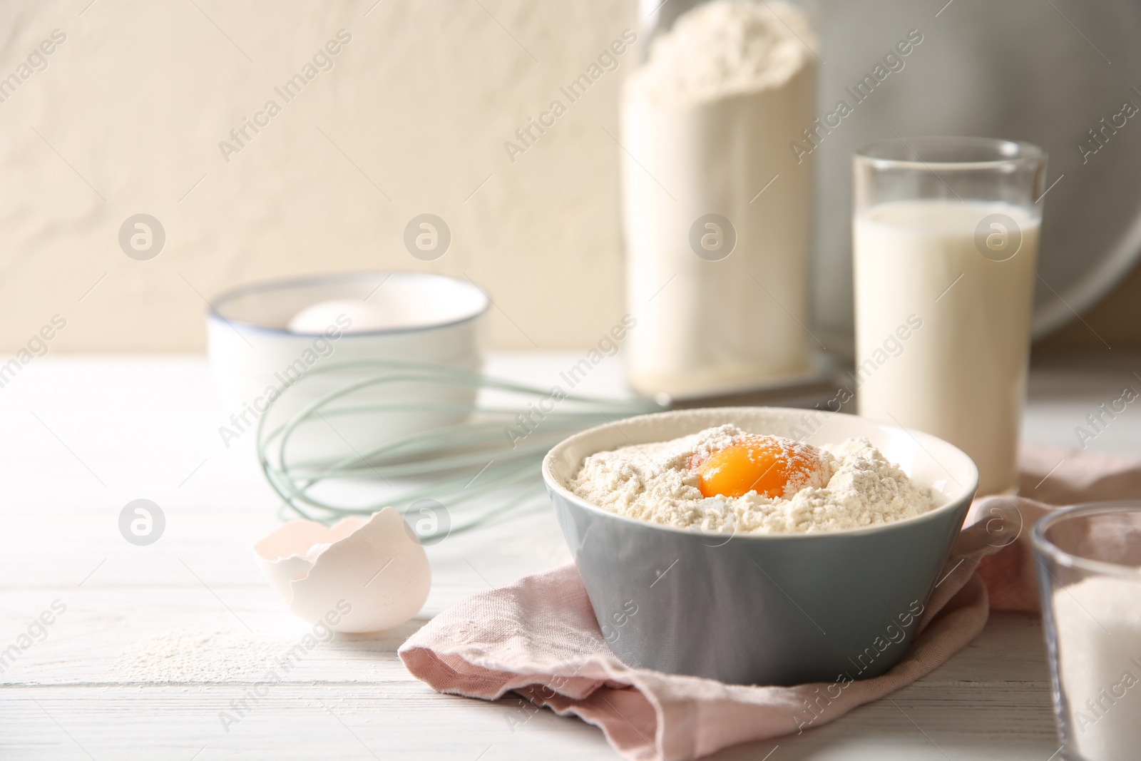 Photo of Making dough. Flour with yolk in bowl on white wooden table, closeup