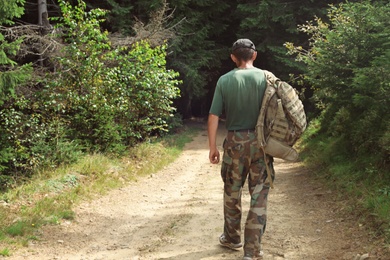 Photo of Tourist with backpack on path walking to forest. Camping season