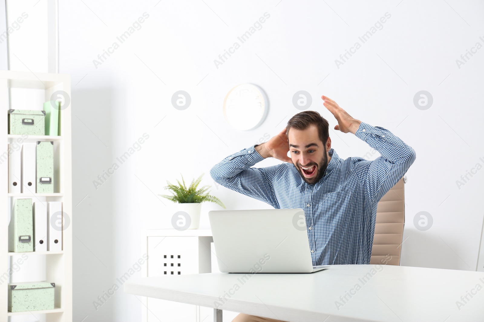 Photo of Emotional young man with laptop celebrating victory in office. Space for text