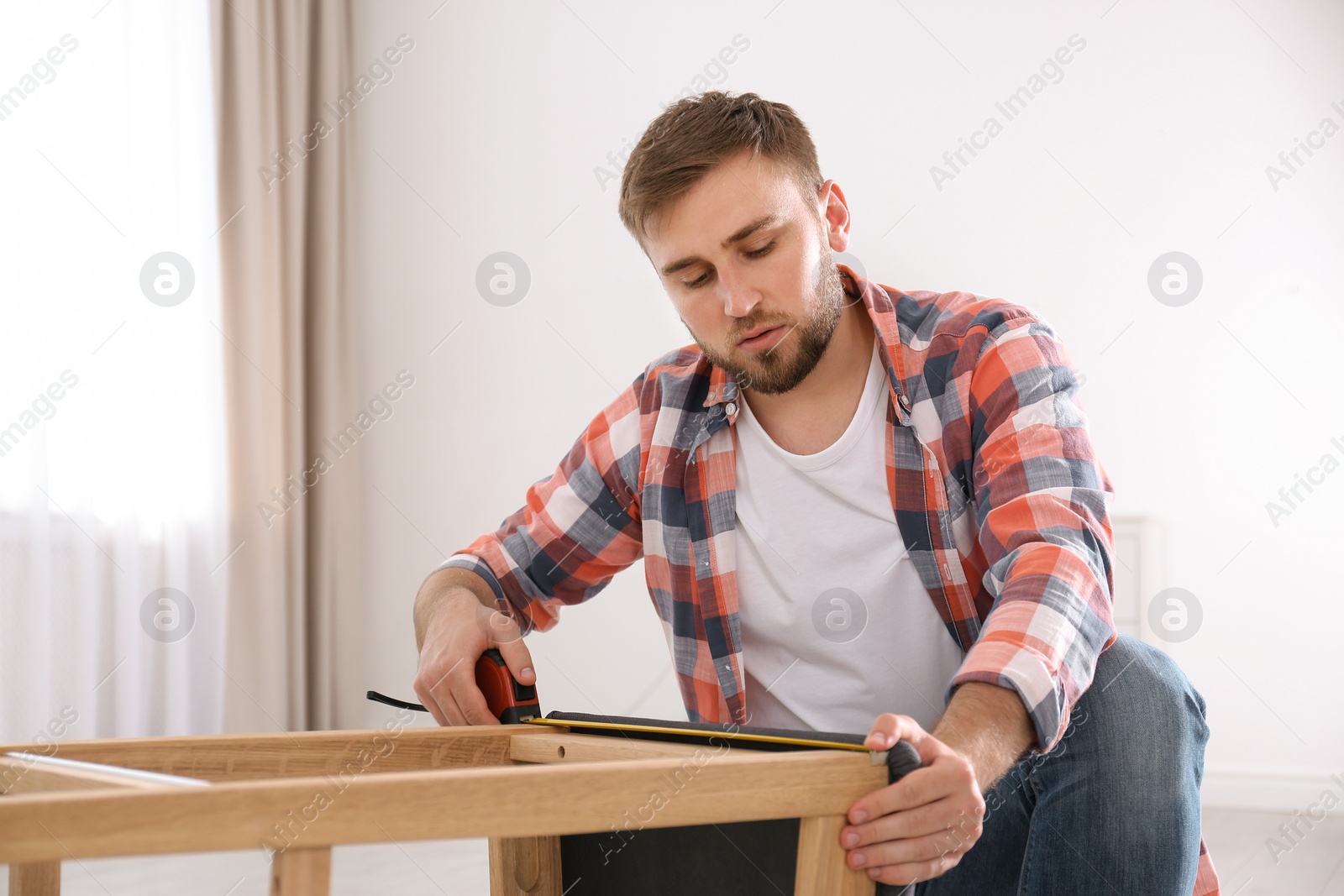 Photo of Young working man using measure tape at home, space for text