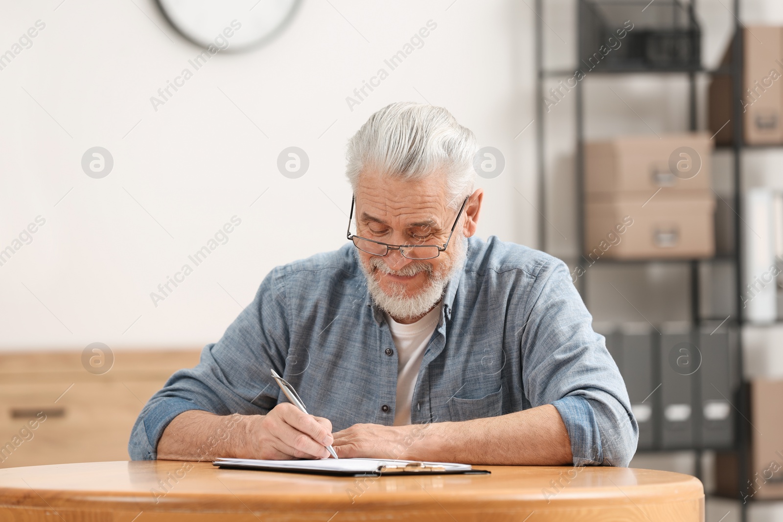 Photo of Senior man signing Last Will and Testament at table indoors