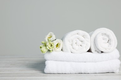 Photo of Soft white towels with flowers on wooden table against grey background, space for text