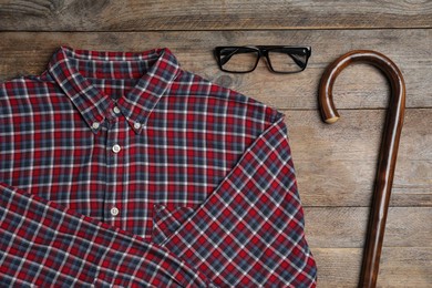 Elegant walking cane, glasses and shirt on wooden table, flat lay