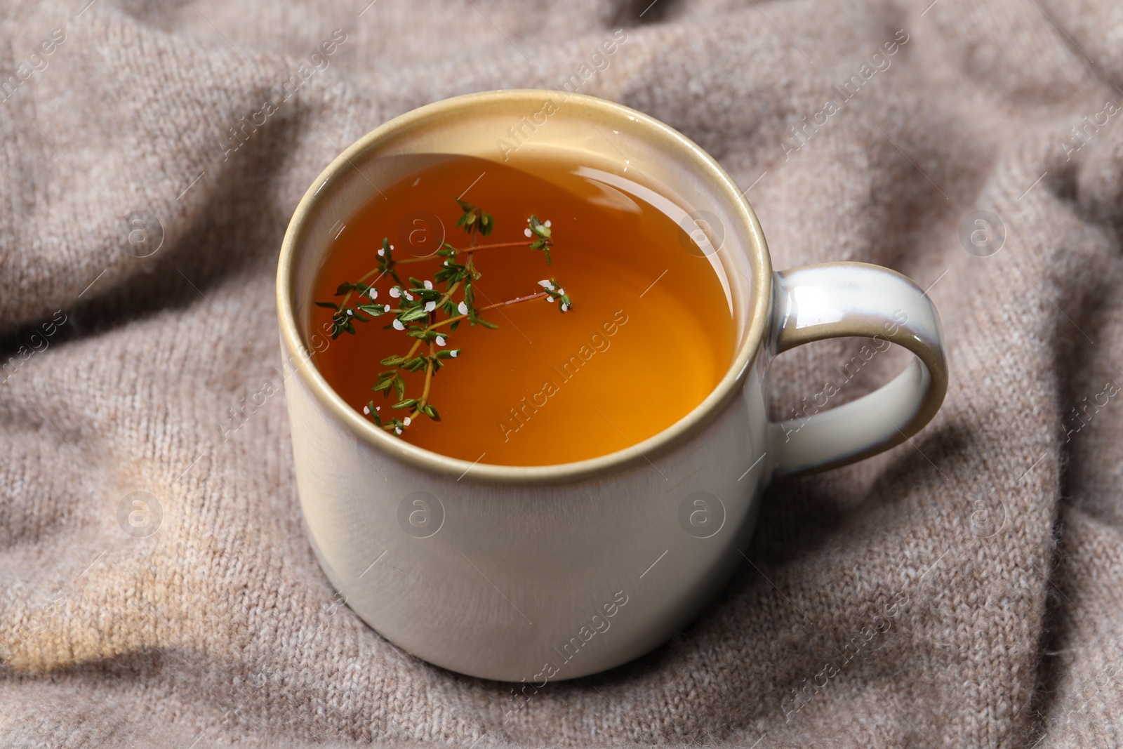 Photo of Cup of aromatic herbal tea with thyme on beige fabric