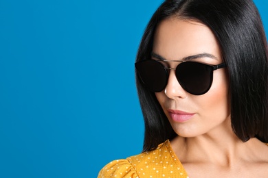 Beautiful woman wearing sunglasses on blue background, closeup. Space for text