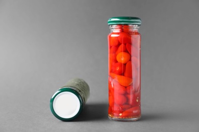 Photo of Jars of pickled red hot piri-piri peppers and capers on grey background