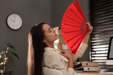 Photo of Woman with hand fan suffering from heat at home. Summer season