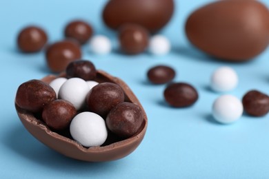 Photo of Tasty chocolate egg with different sweets inside on light blue background, closeup. Space for text