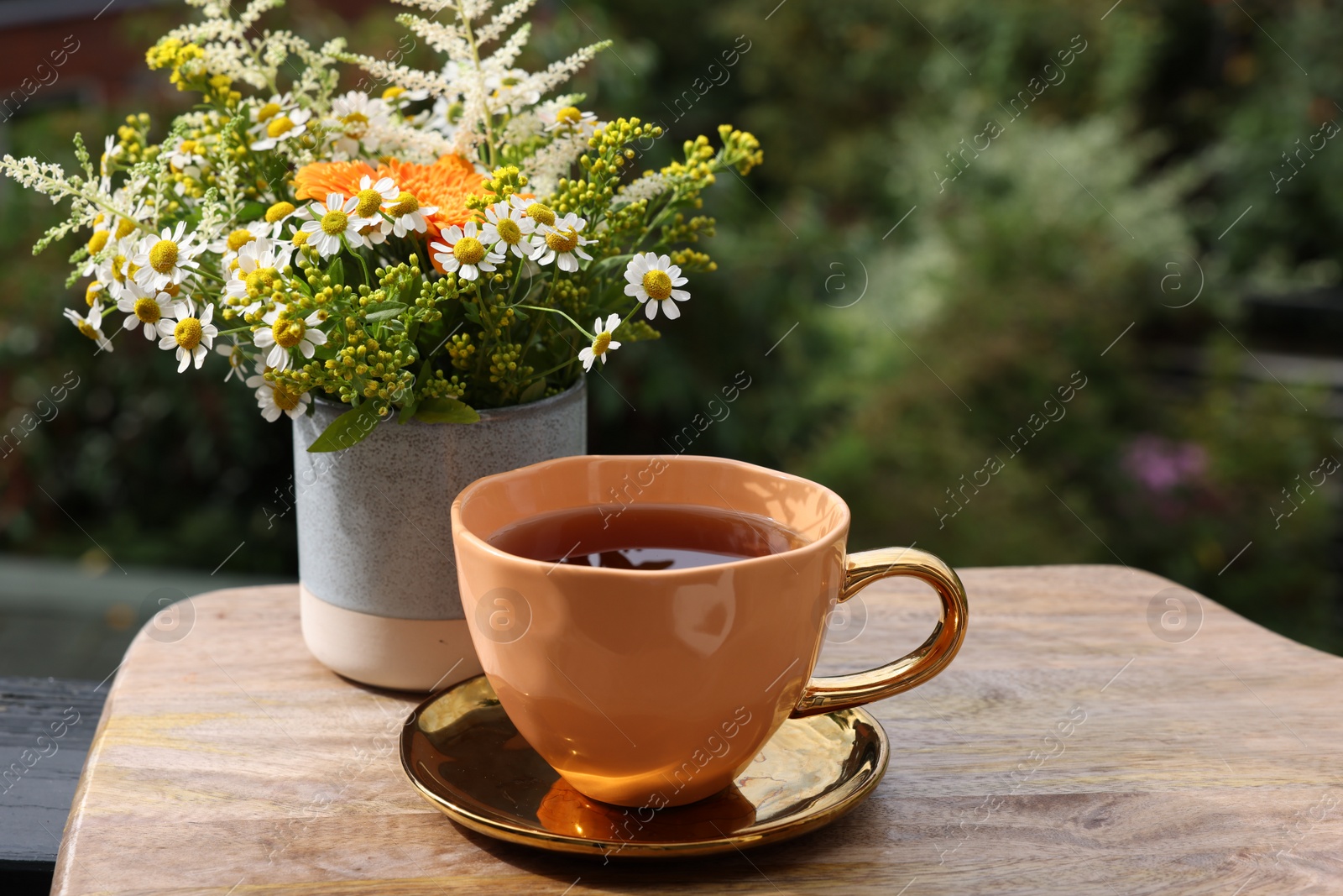 Photo of Cup of delicious chamomile tea and fresh flowers outdoors on sunny day