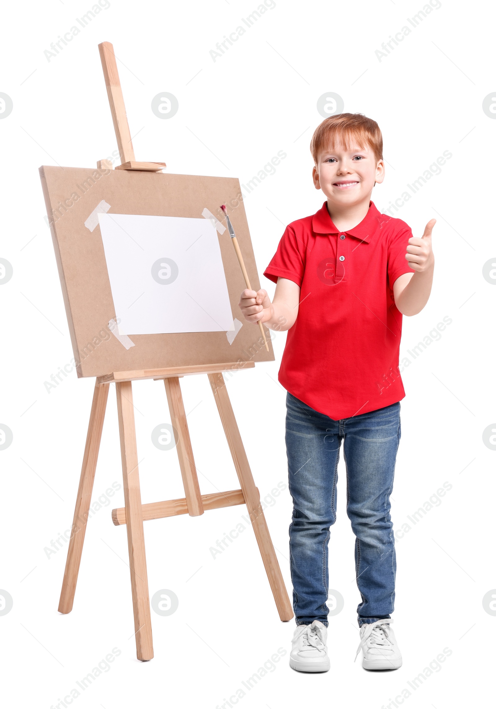 Photo of Little boy with brush near easel with canvas showing thumbs up against white background. Creative hobby