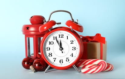 Alarm clock with Christmas decor on light blue background. New Year countdown