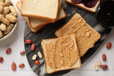 Photo of Delicious toasts with peanut butter, nuts and jam on white tiled table, top view