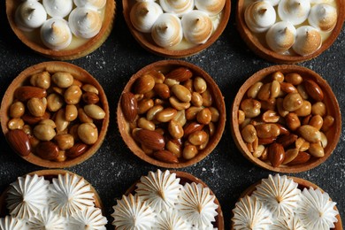 Many different tartlets on black textured table, flat lay. Tasty dessert