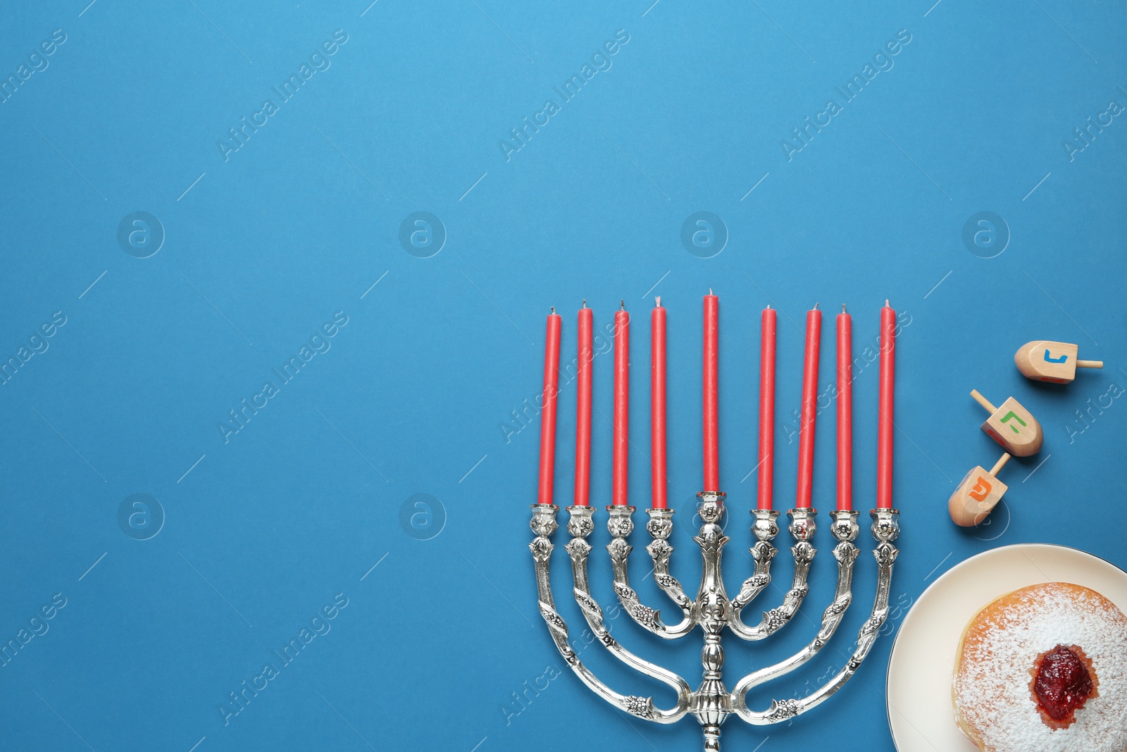 Photo of Hanukkah traditional menorah, candles, doughnut, dreidels with letters He, Pe, Nun, Gimel on blue background, flat lay. Space for text