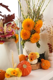 Composition with small pumpkins and beautiful flowers on white window sill indoors