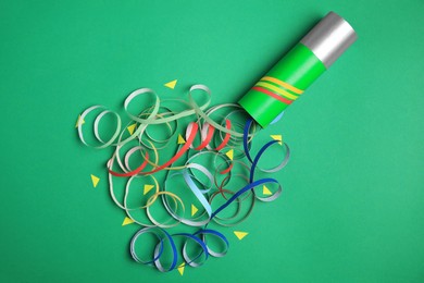 Photo of Beautiful serpentine and confetti bursting out of party popper on green background, flat lay