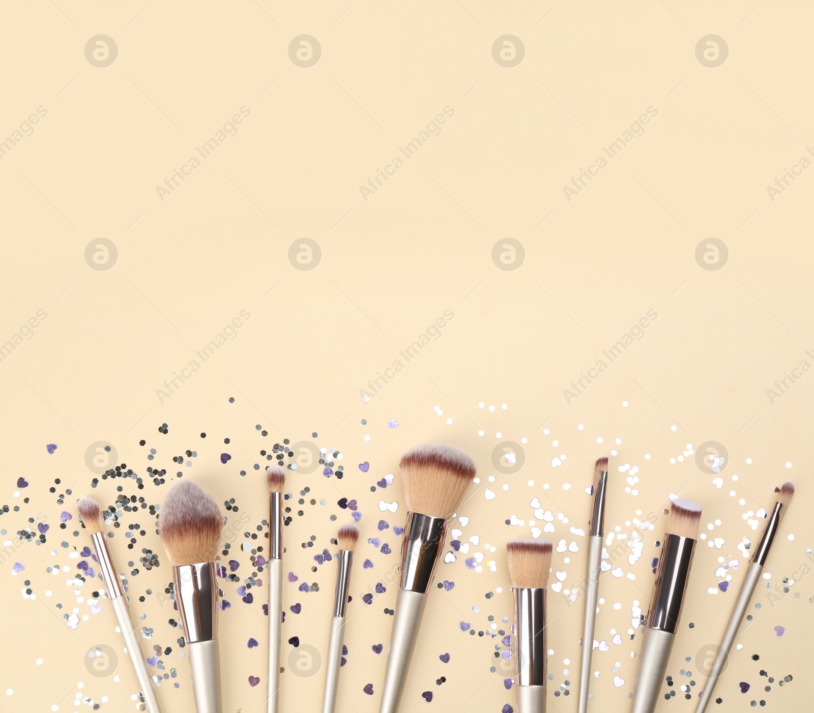 Photo of Different makeup brushes and shiny confetti on beige background, flat lay. Space for text