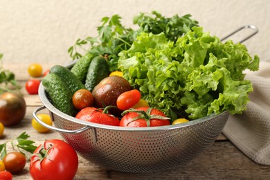 Wet vegetables in colander on wooden table, closeup