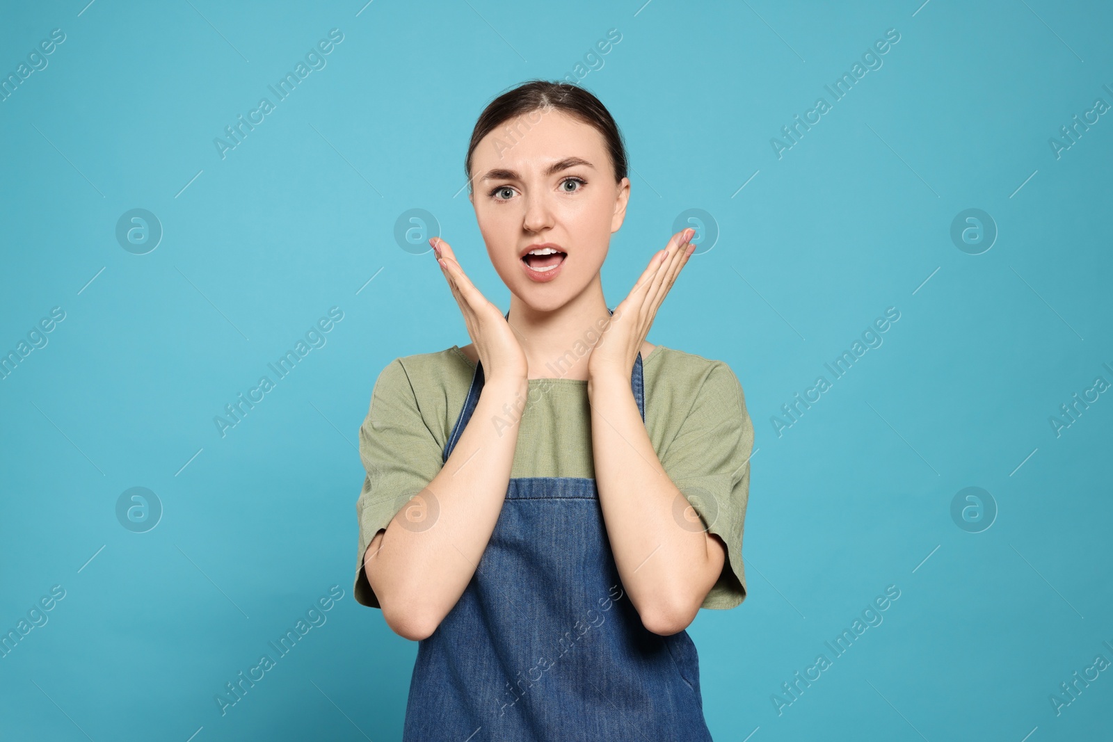 Photo of Beautiful young woman in clean denim apron on light blue background