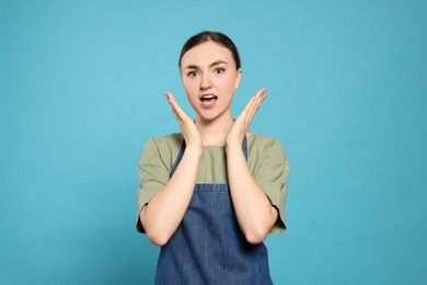 Beautiful young woman in clean denim apron on light blue background