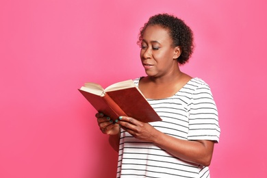 Photo of Portrait if mature African-American woman reading book on pink background