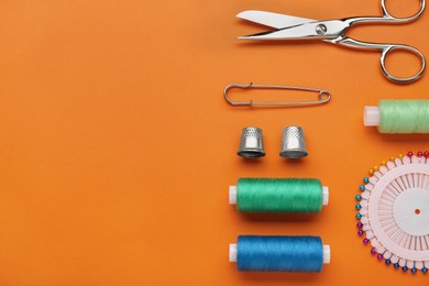 Flat lay composition with thimbles and different sewing tools on orange background, space for text