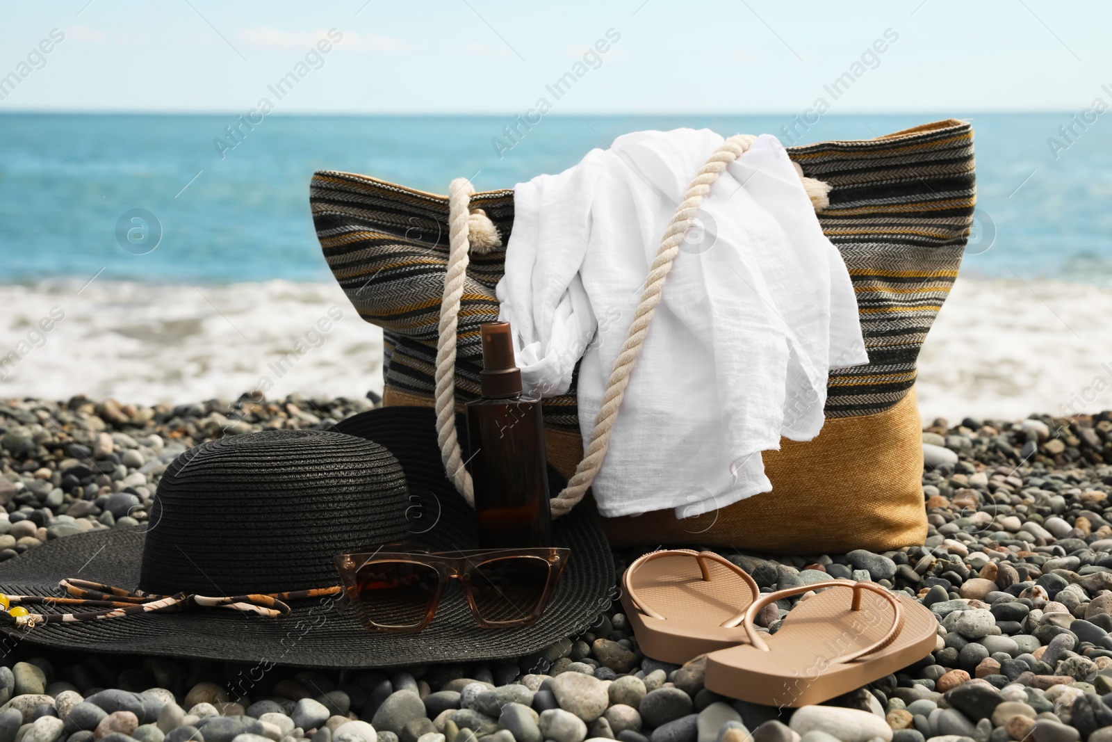 Photo of Beautiful hat with sunglasses, bag and flip flops near sea on pebble beach