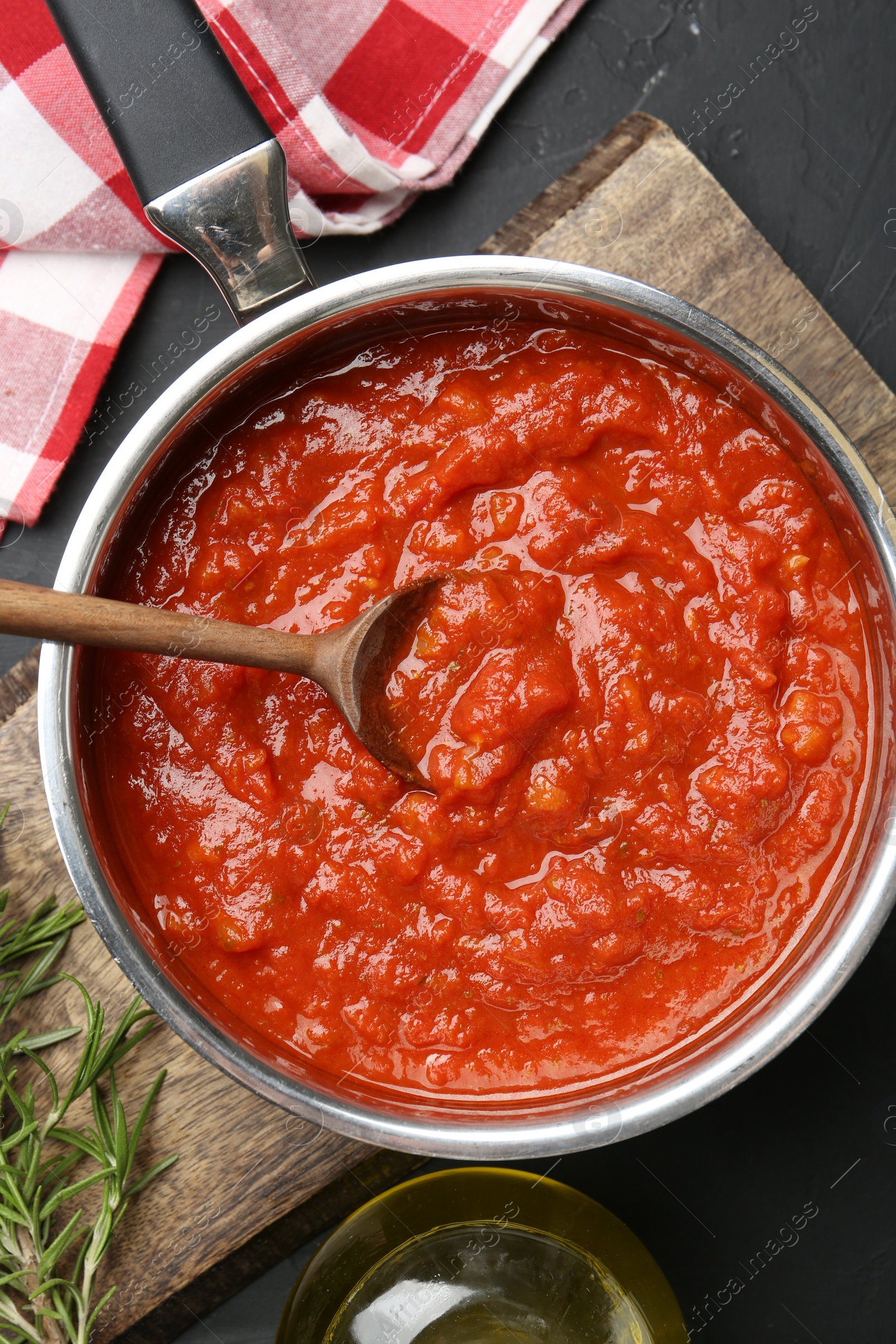 Photo of Homemade tomato sauce in pot, spoon and fresh ingredients on dark table, flat lay