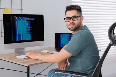 Happy young programmer working at desk in office