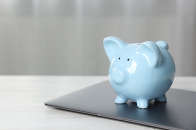 Photo of Piggy bank and laptop on white table indoors. Space for text