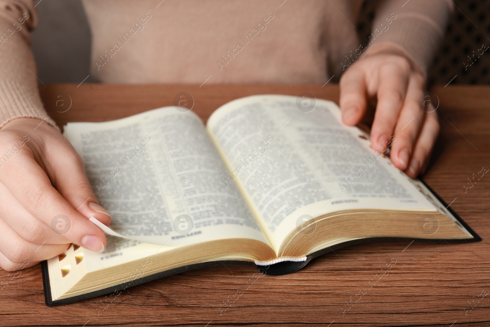 Photo of Woman reading Bible at wooden table, closeup